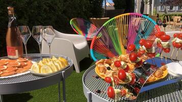 Mesa al aire libre con comida y bebidas, rodeada de sillas coloridas.