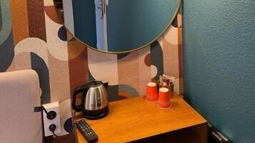 Un baño con un espejo redondo, un lavamanos con una tetera y dos tazas rojas.