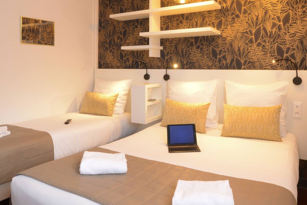 A hotel room with two beds, a laptop on one bed, and a wall with a leaf pattern.