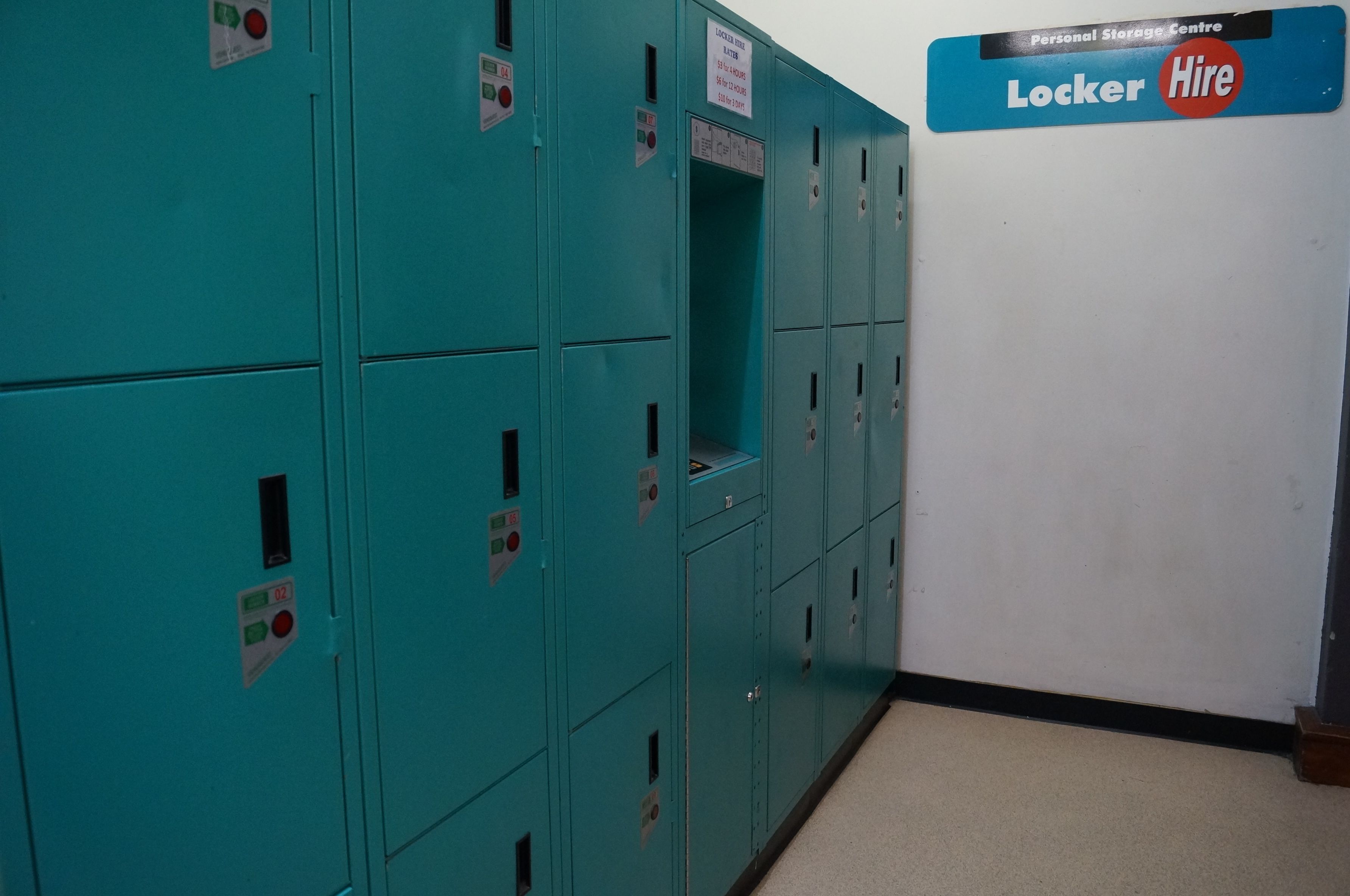 Een rij turquoise kleedhokjes met een bord waarop een persoonlijke opslagruimte staat aangegeven, en een bord met de tekst 'Huurhokjes'.