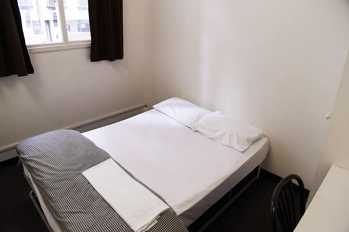 A single bed with white bedding, a checkered blanket, and a black chair.