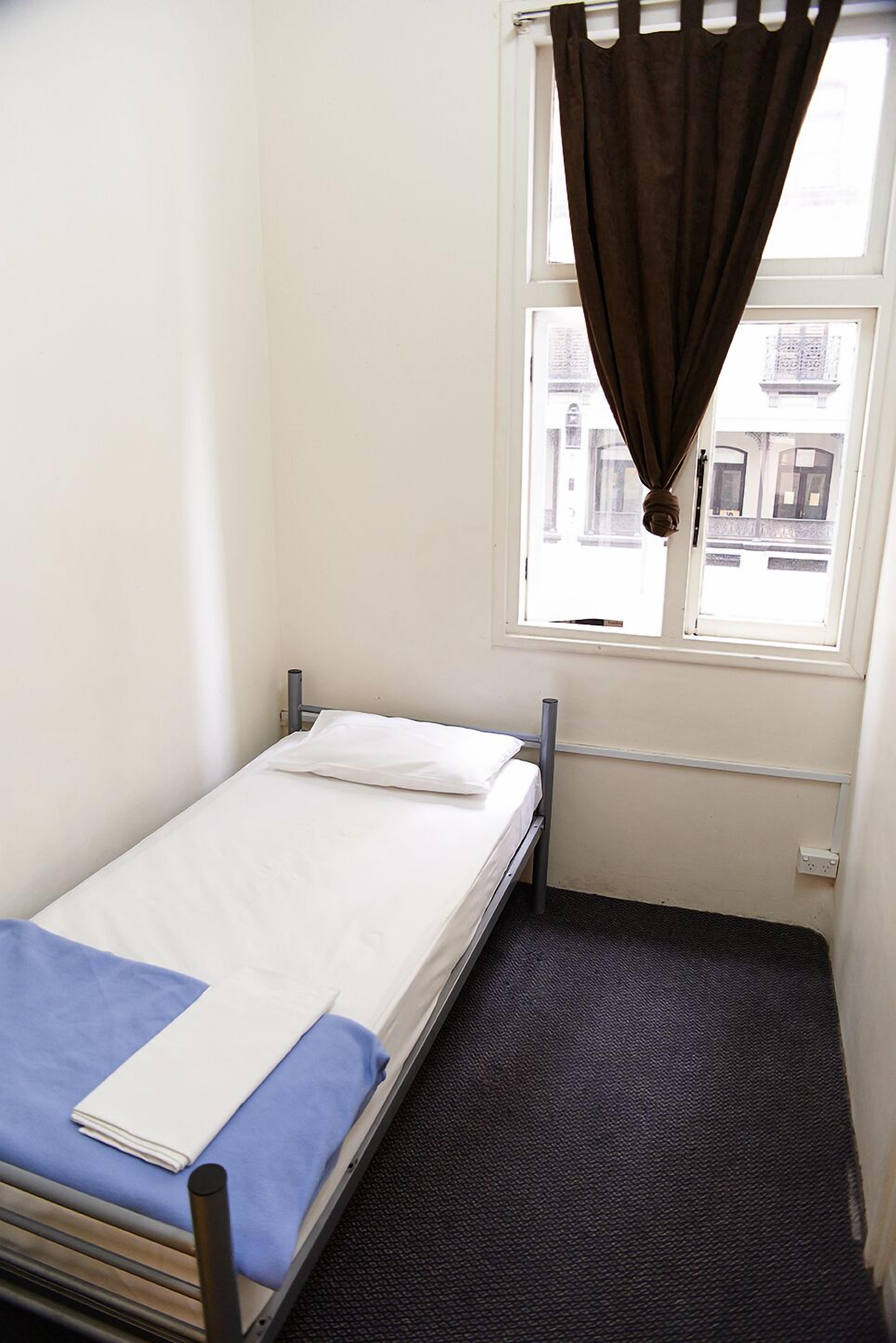 Une petite chambre avec un lit simple, une fenêtre et une vue sur les bâtiments environnants.