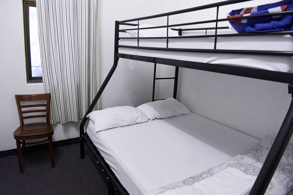 A bunk bed with white bedding, a wooden chair, and a window with curtains.