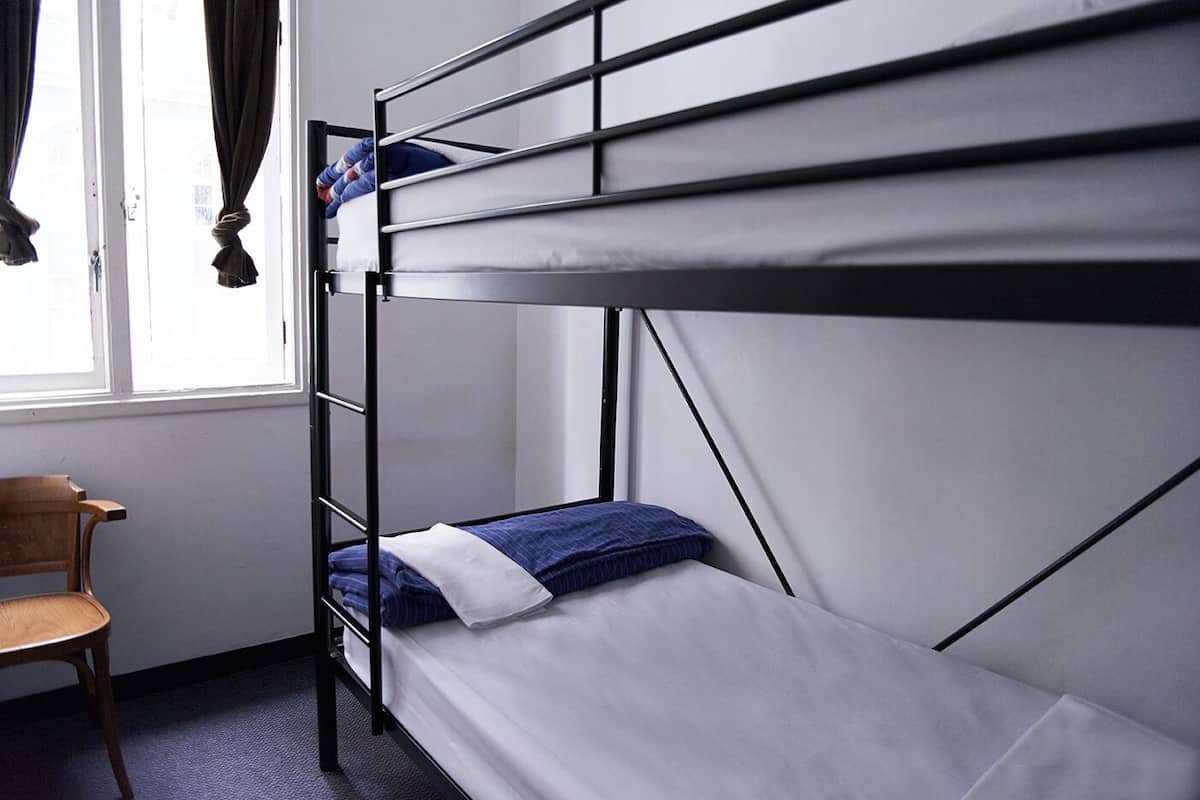 A bunk bed with a wooden chair beside it, a window with curtains, and a white wall.