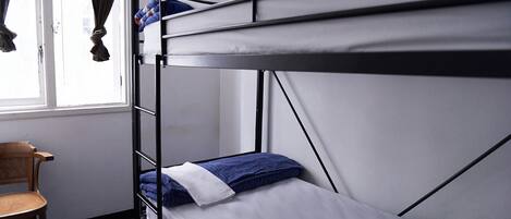 A bunk bed with a wooden chair beside it, a window with curtains, and a white wall.