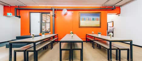 A conference room with tables and benches, orange walls, a painting, and a door.