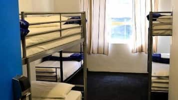 A dormitory room with bunk beds, a window with curtains, and a ceiling fan.