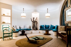 A modern living room with a teal armchair, blue sofas, a wooden coffee table, and a decorative branch sculpture. - Dolce Vita Boutique Hotel (Arzachena)