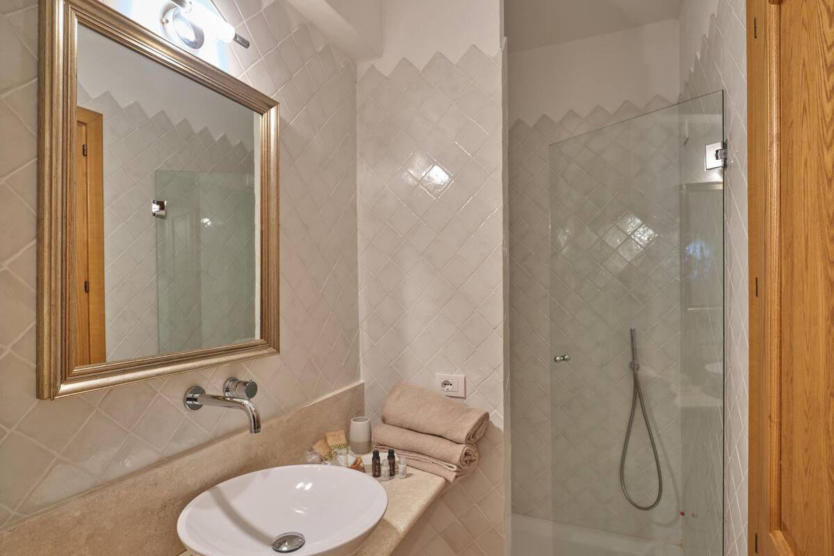 Un baño con un lavamanos blanco, un espejo, una toalla y un box de ducha de vidrio.