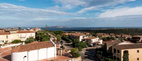 A coastal town with traditional architecture, a central square, and a view of the sea and distant mountains.