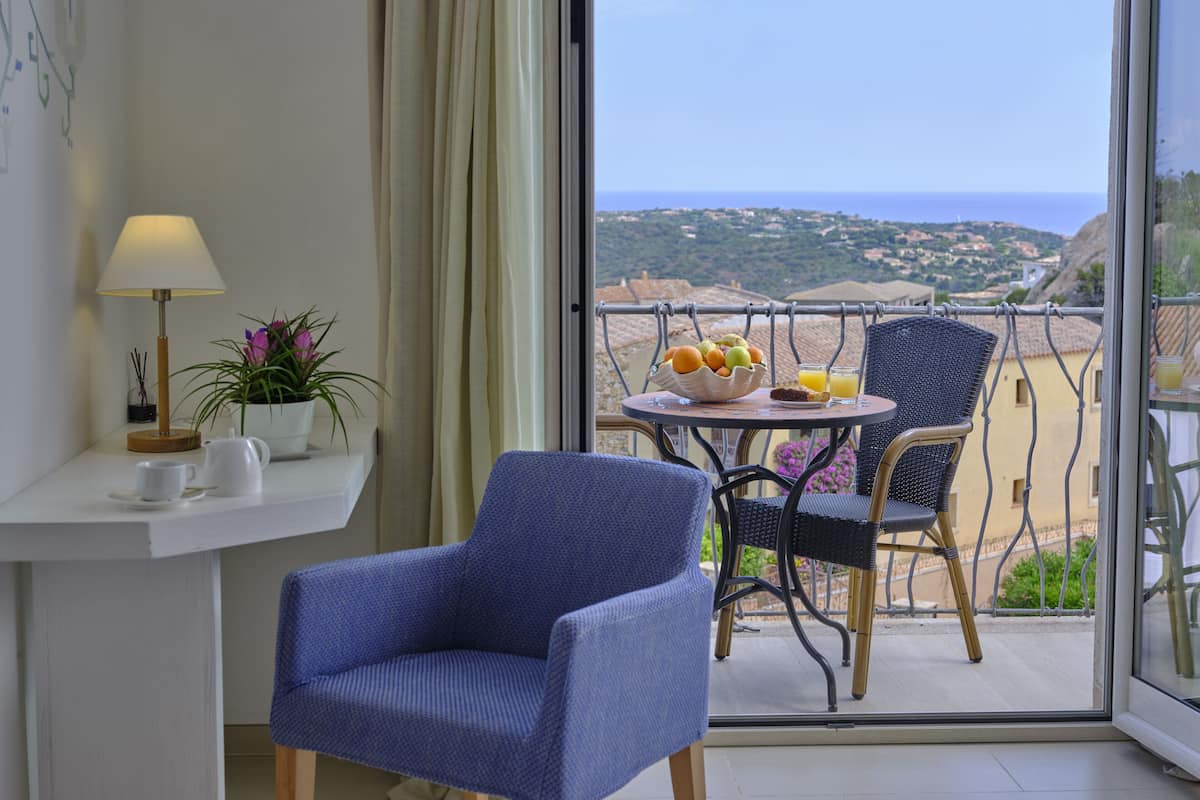 Un balcón con una mesa preparada para el desayuno, una silla, una lámpara y vistas al paisaje.