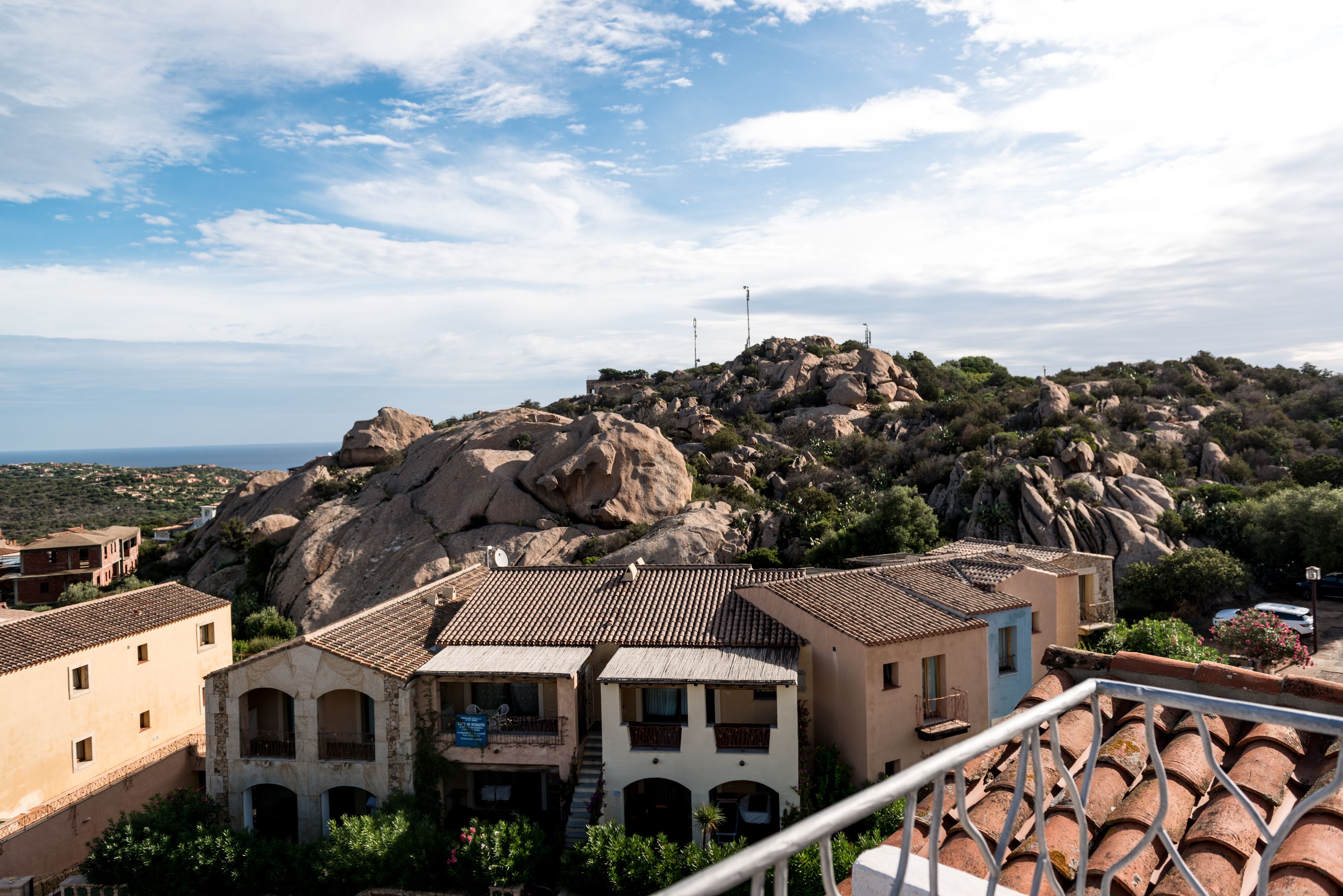Un pueblo costero con edificios de piedra tradicionales, tejados de teja y una colina rocosa destacada al fondo.