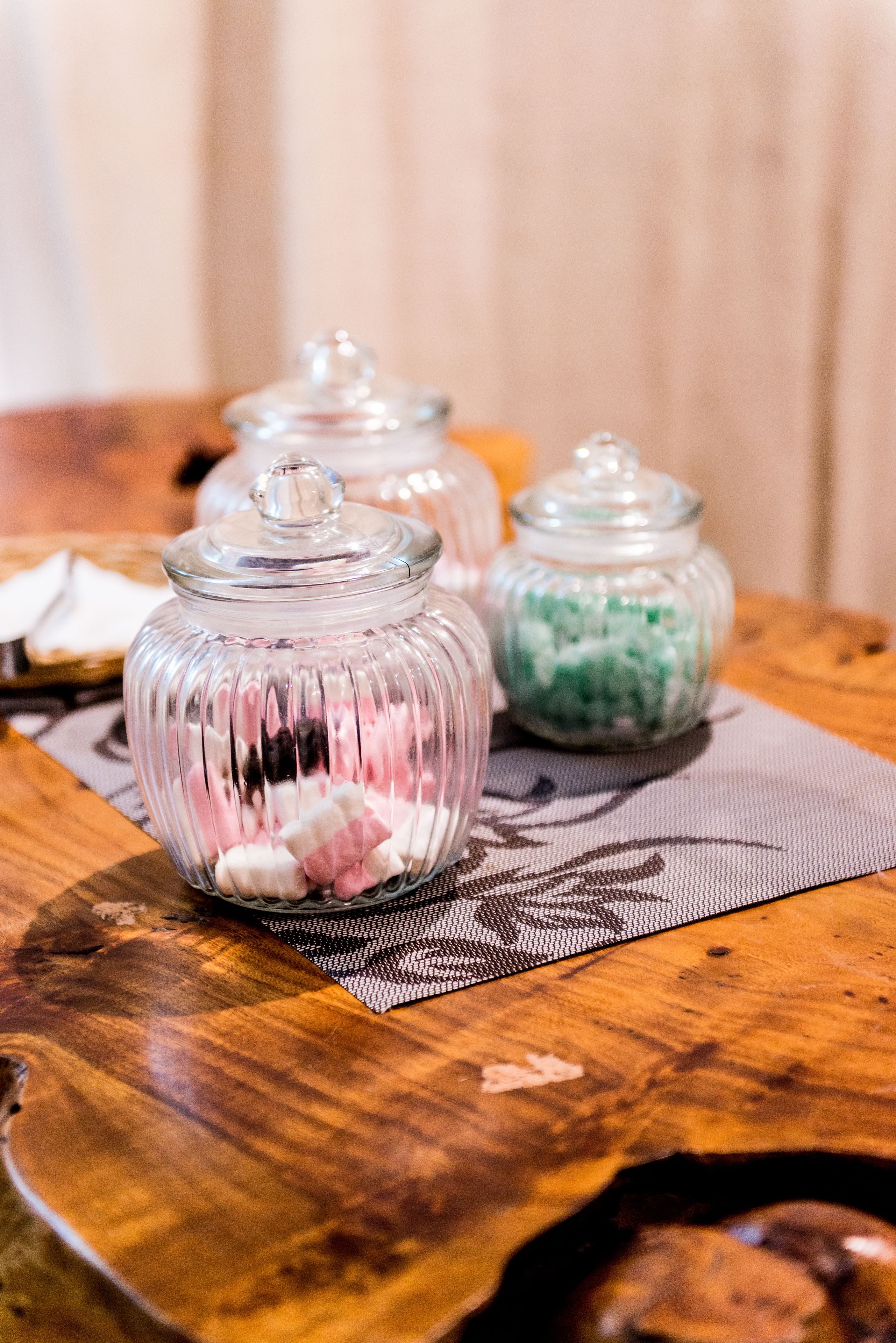 Tre glas med låg på en træbordplade, fyldt med forskelligfarvede slik.