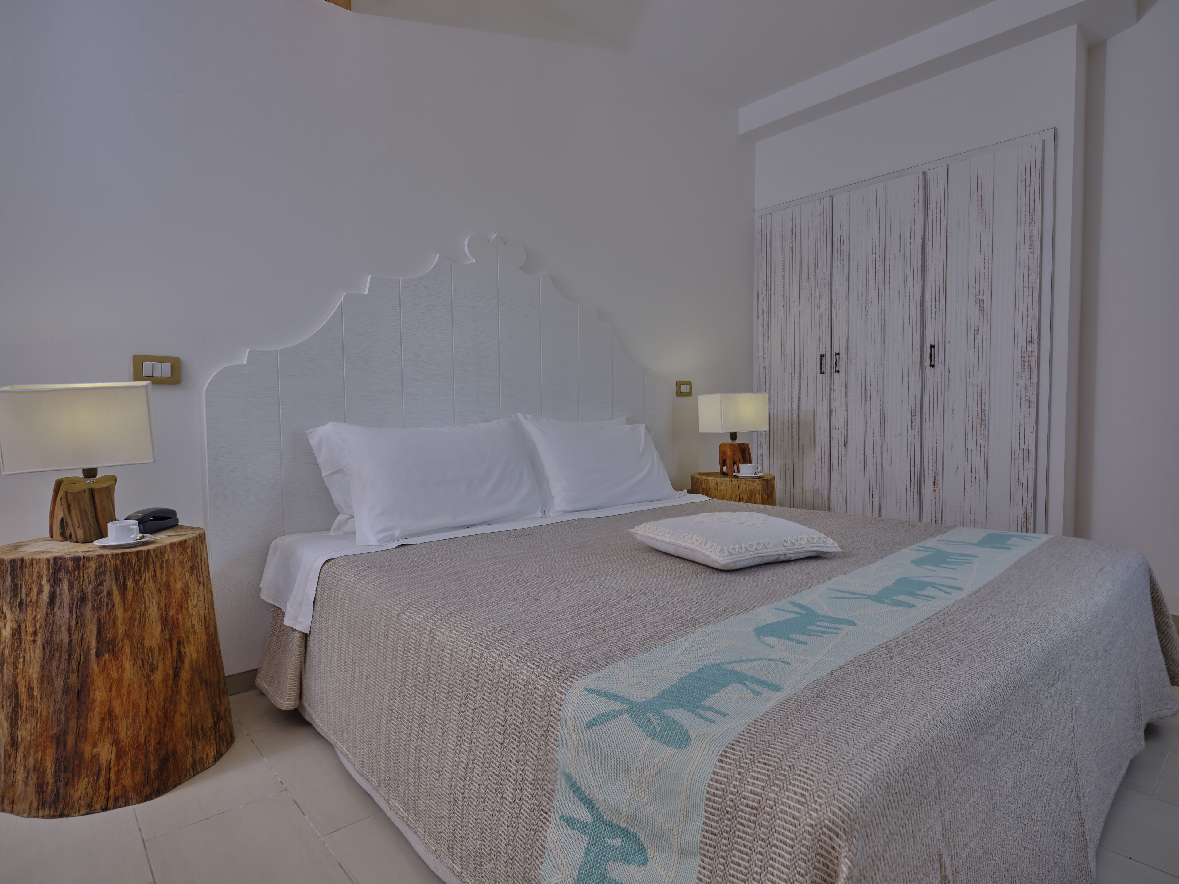 Quarto com uma cama, duas mesas de cabeceira, um guarda-roupa e um interruptor de luz fixado na parede.