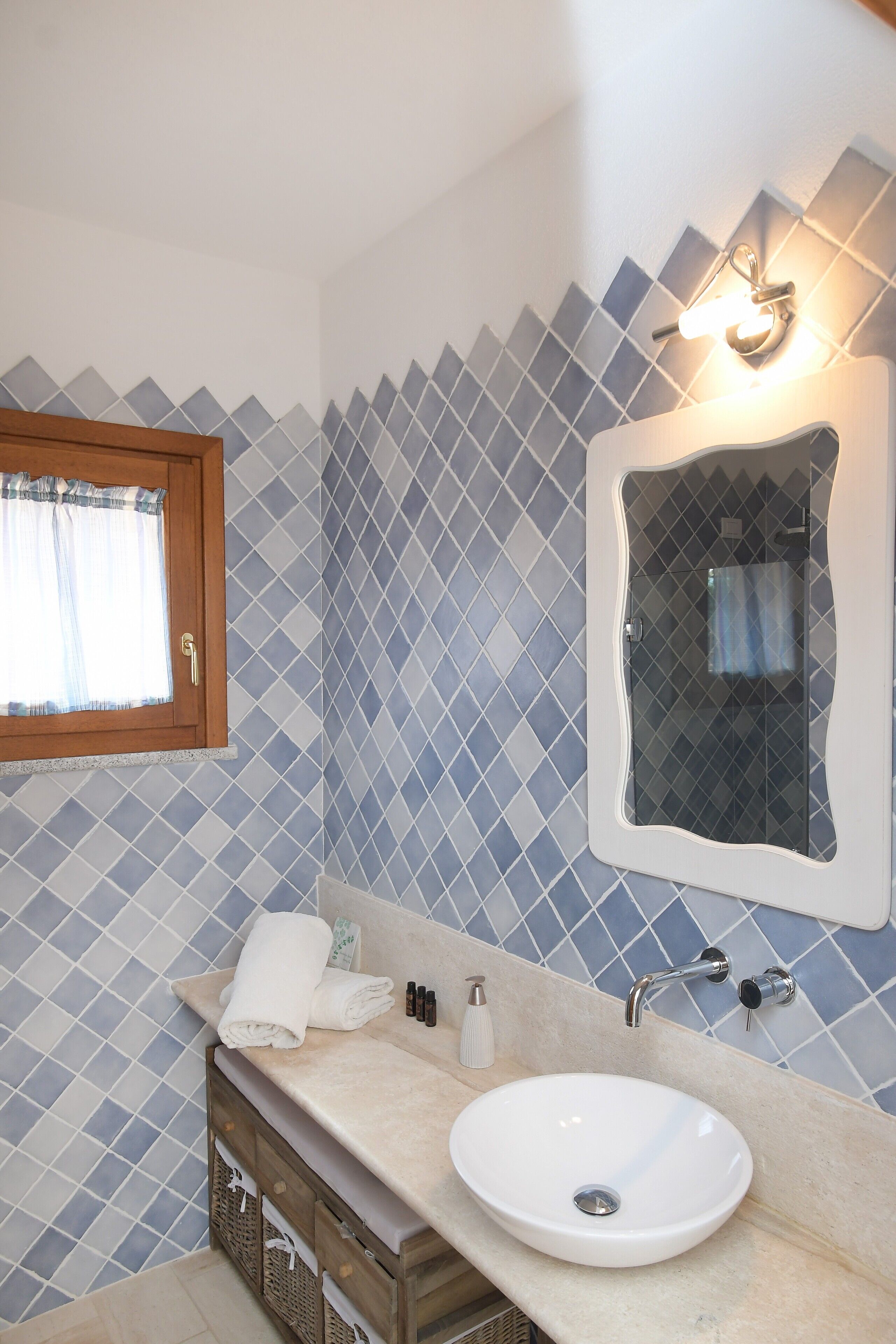 A bathroom with a tiled wall, a sink, a mirror, and a window with curtains.