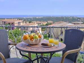 A table with a fruit bowl, two glasses of orange juice, and a plate with food on a balcony overlooking a coastal town. - Dolce Vita Boutique Hotel (Arzachena)