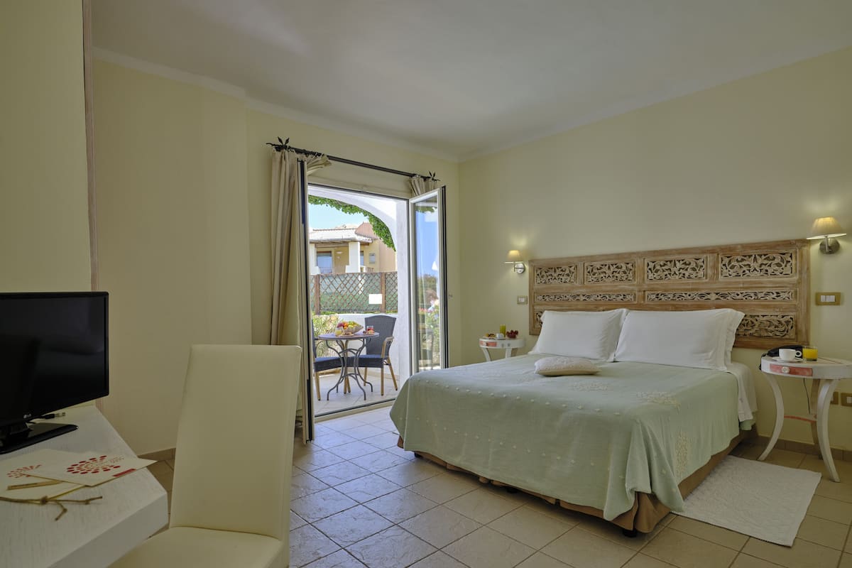 Habitación de hotel con cama, televisor, mesa con lámpara y vista al exterior.