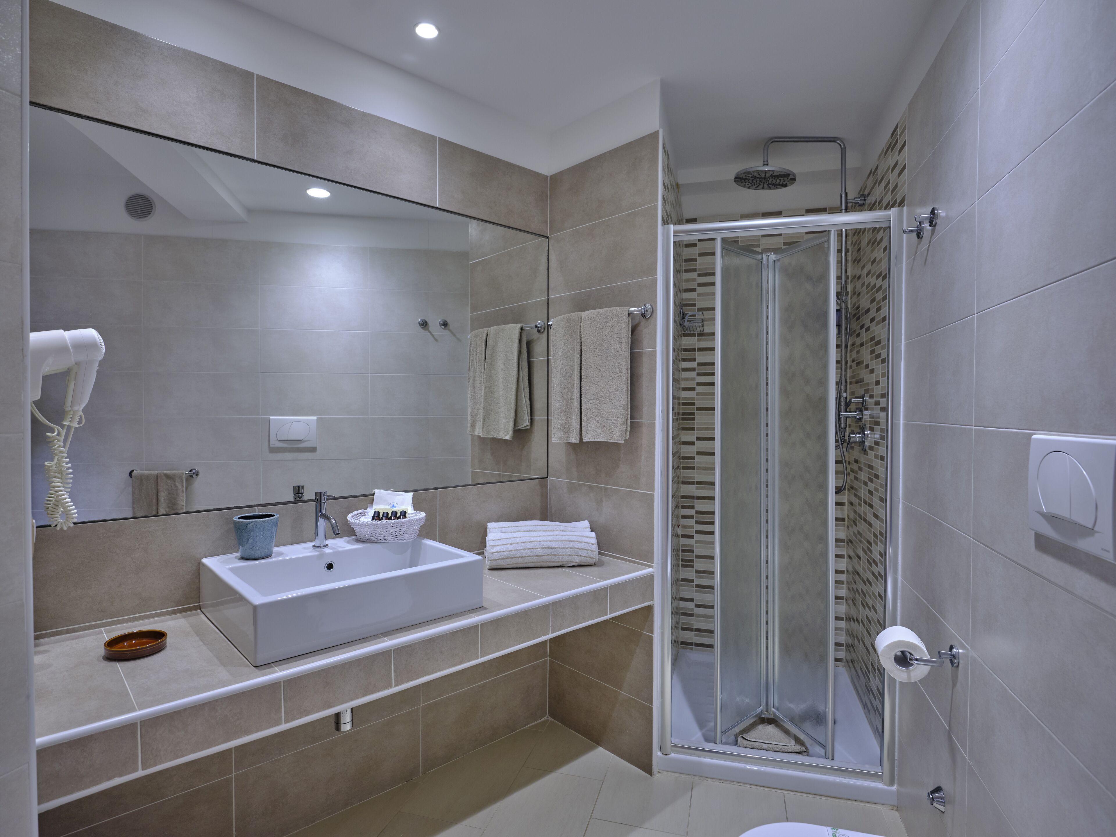 A modern bathroom with a large mirror, a sink, a shower, and a toilet.