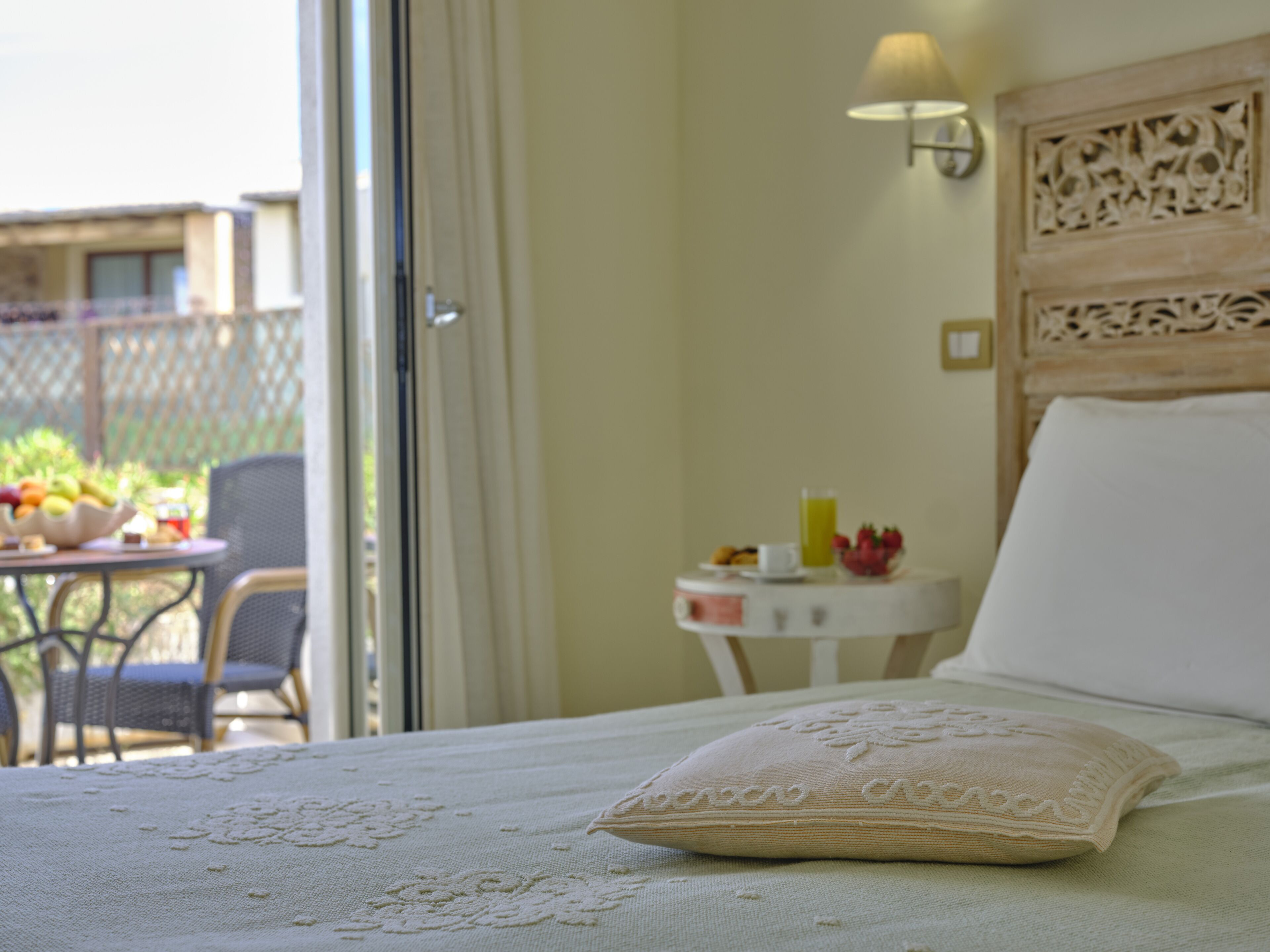 A bedroom with a bed, a nightstand, a lamp, and a view of the outside balcony.