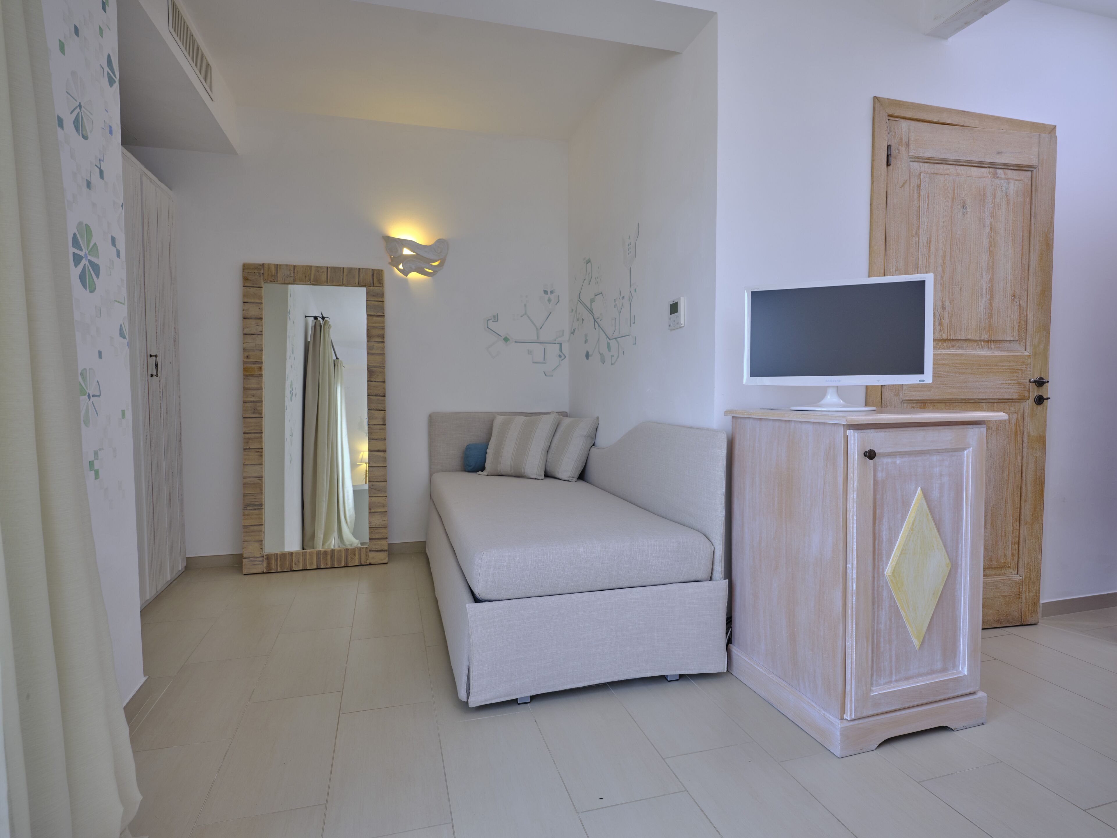 Ein Schlafzimmer mit Bett, Kleiderschrank, Fernseher auf einem Schrank und einer Wandleuchte.