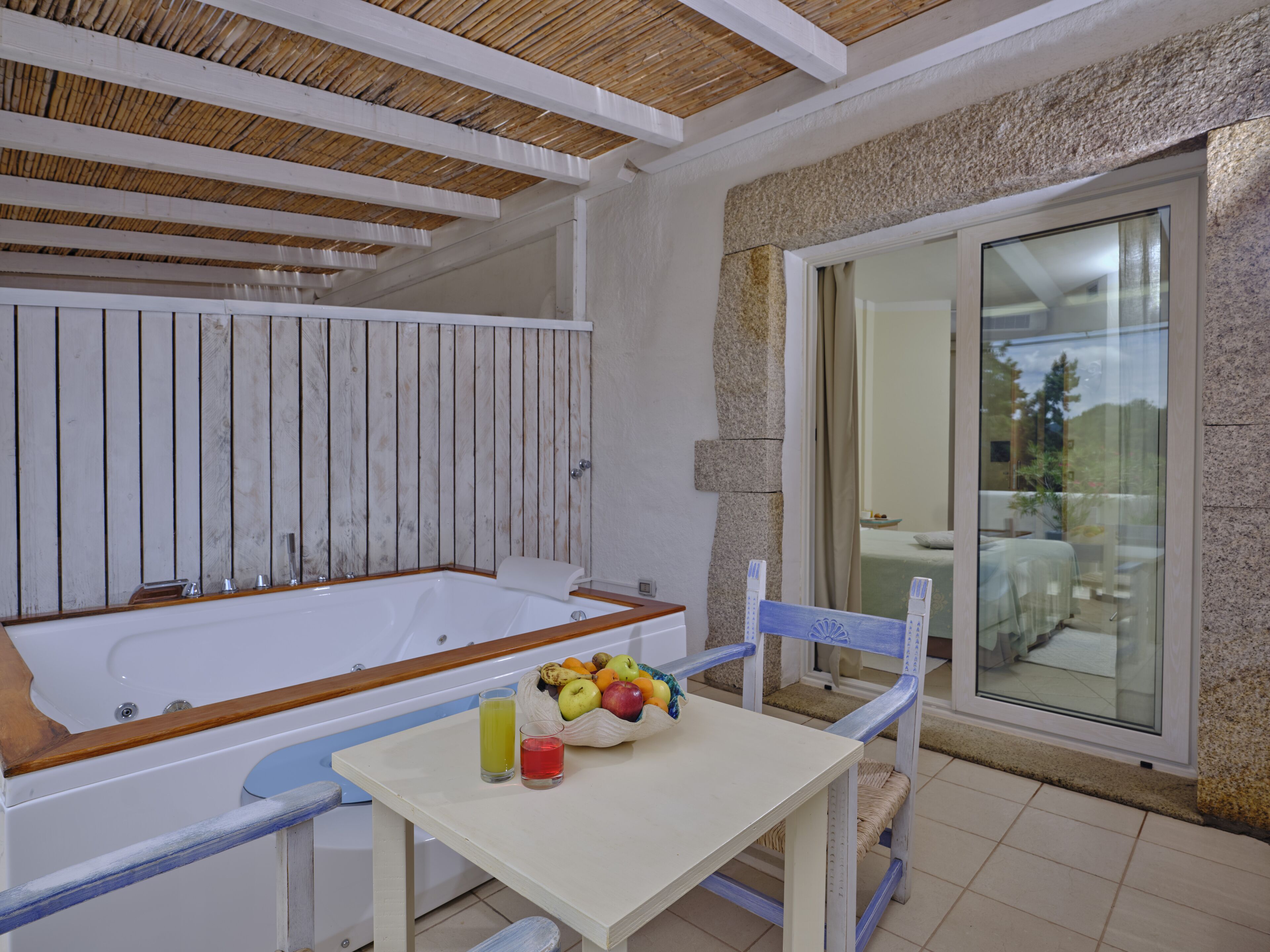 A bathroom with a bathtub, a table with fruit and drinks, and a chair.