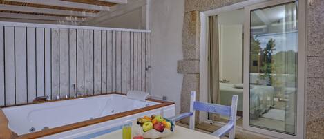 A bathroom with a bathtub, a table with fruit and drinks, and a chair.