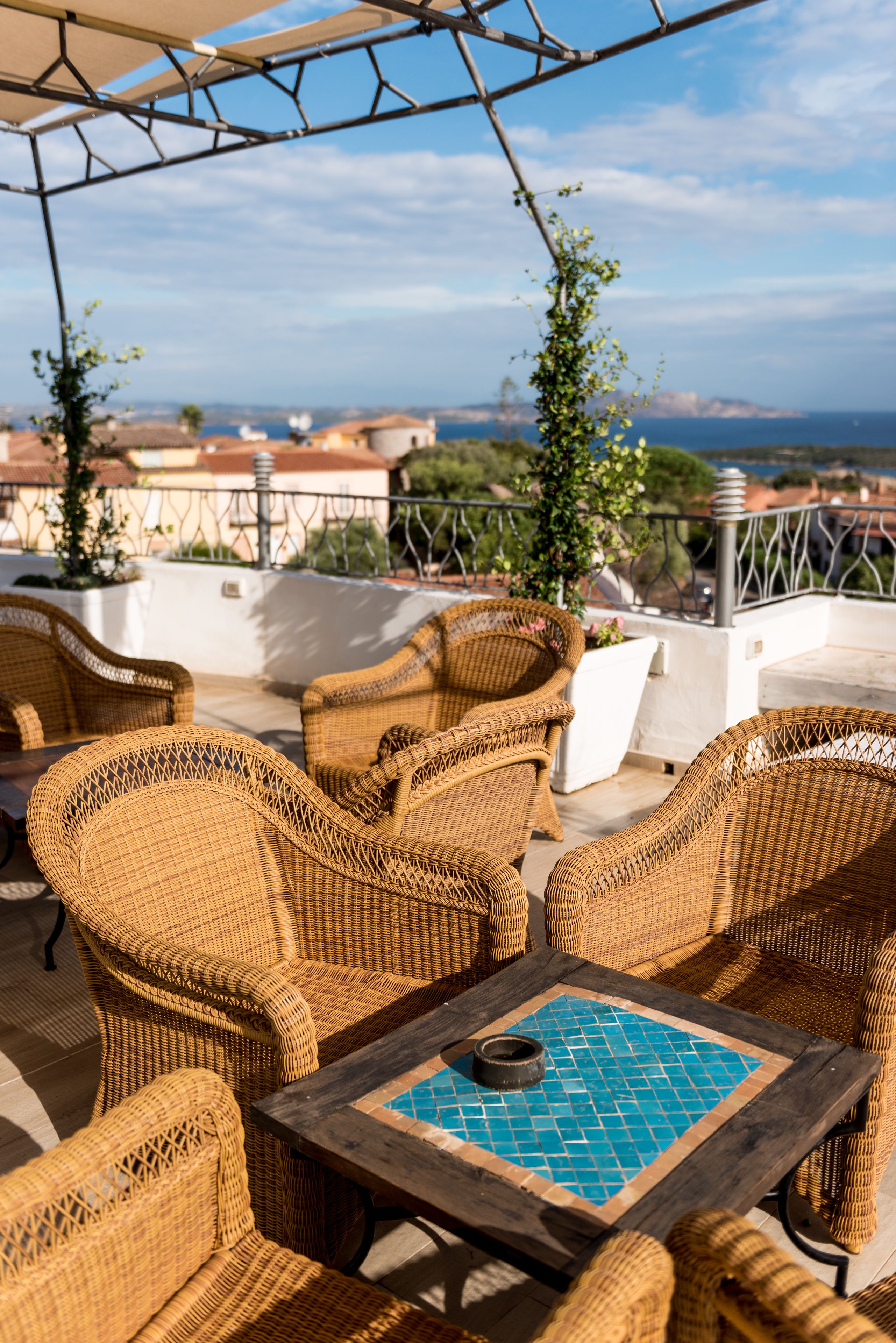 Mueble de mimbre en una terraza con vista al mar y edificios al fondo.