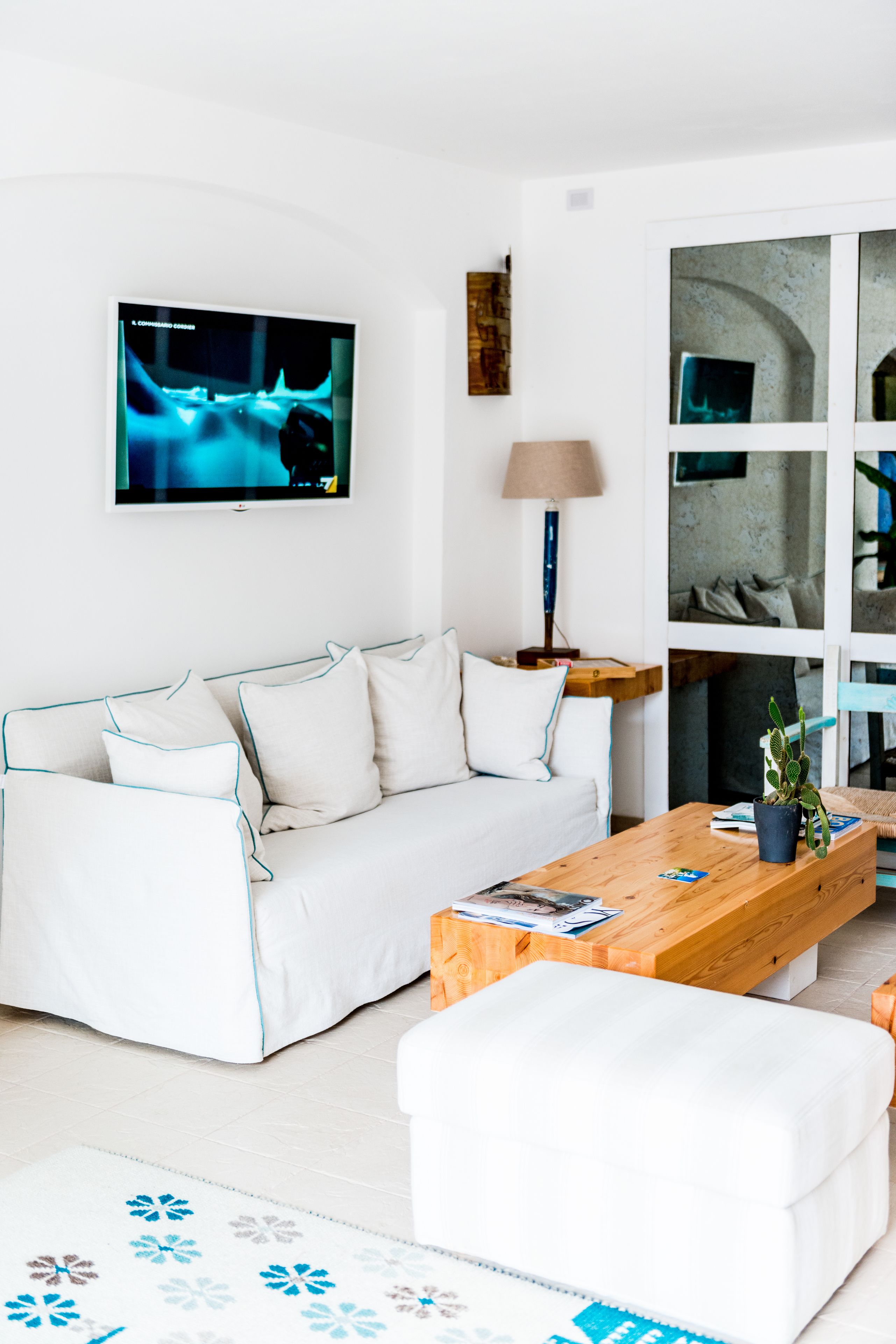 A modern living room with a white sofa, a wooden coffee table, and a TV mounted on the wall.