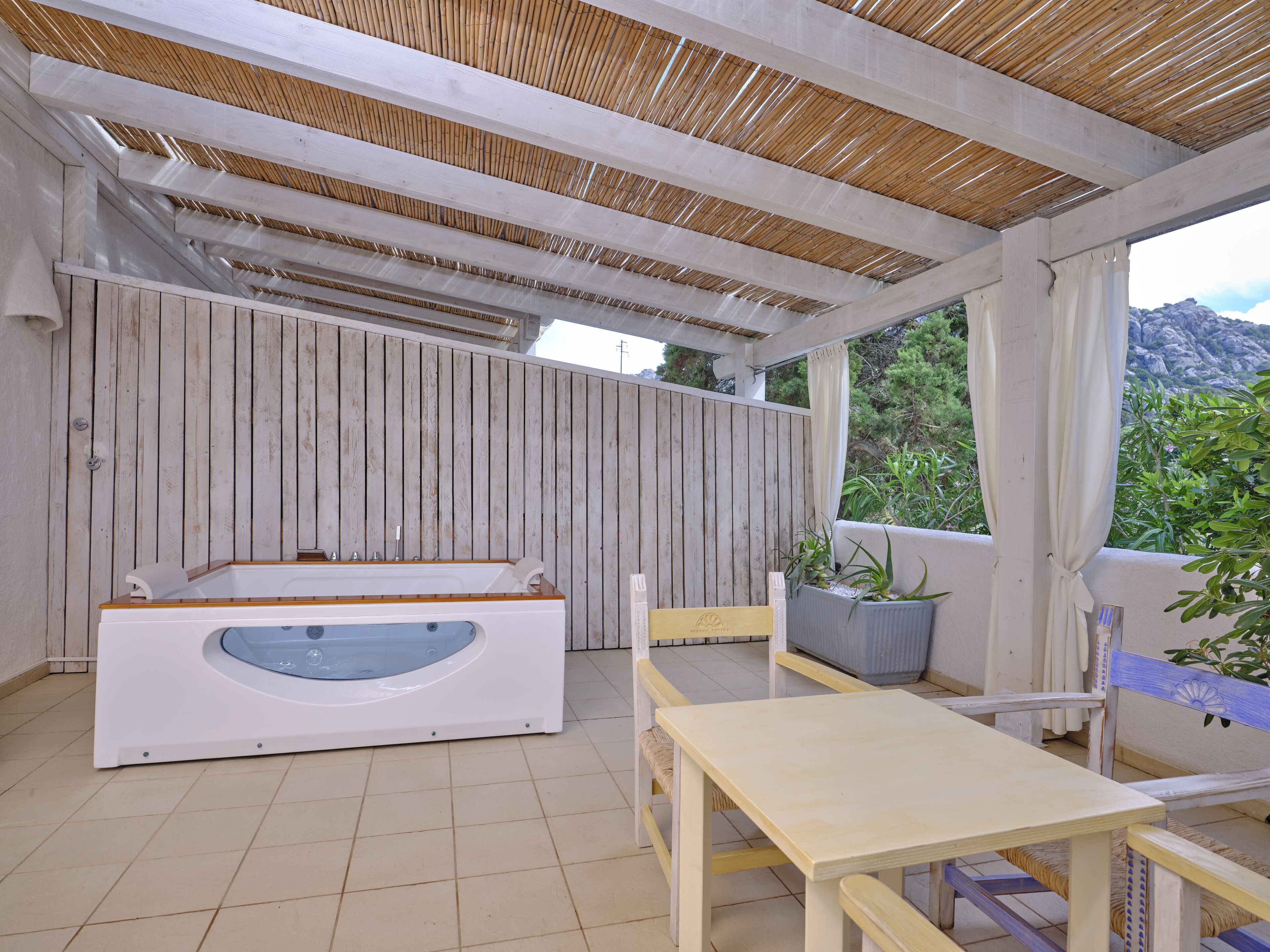 A covered outdoor area with a wooden bench, a table, and a hot tub.