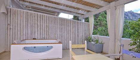 A covered outdoor area with a wooden bench, a table, and a hot tub.