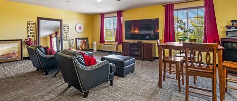A living room with a ceiling fan, a TV, a dining table with chairs, and a large window with curtains.