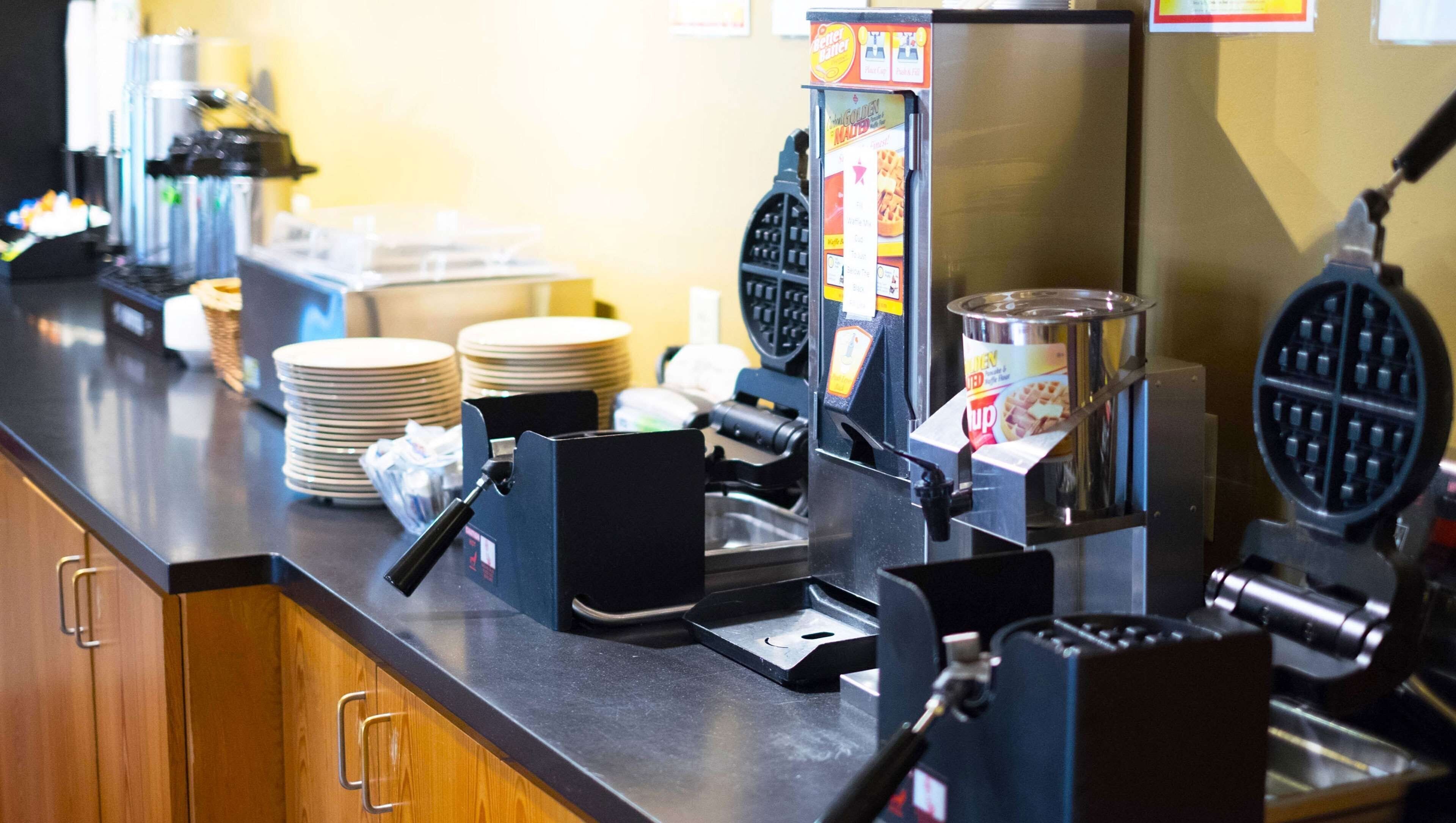 A breakfast station with waffle makers, a coffee machine, and stacked plates.
