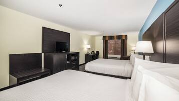 A hotel room with two beds, a desk, a TV, and a window with blinds.