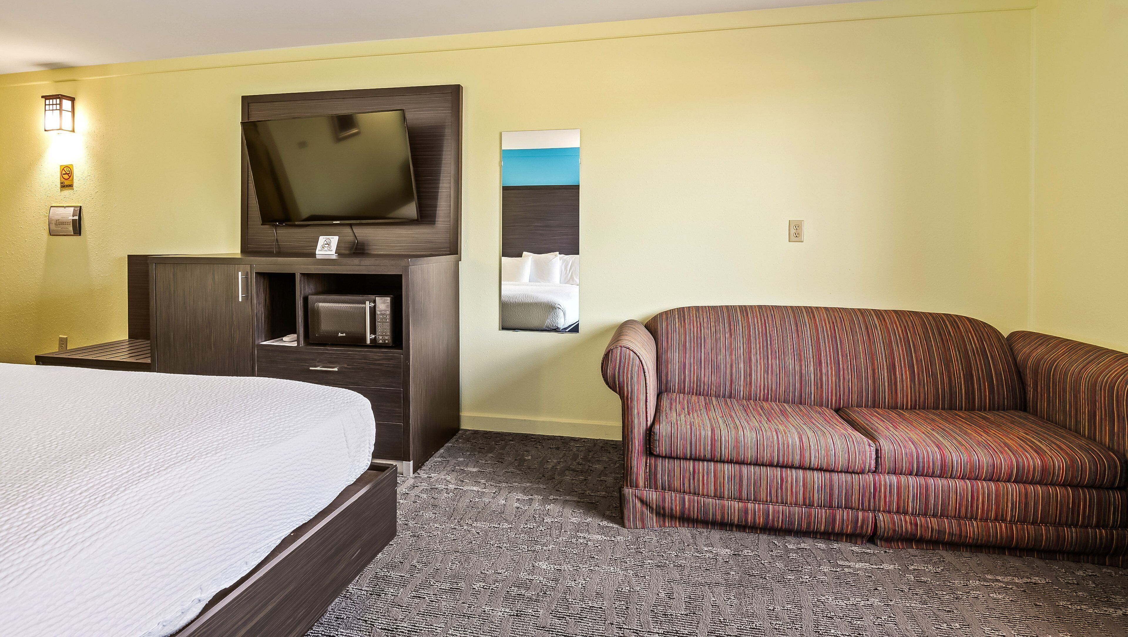 Ein Hotelzimmer mit einem Bett, einem Fernseher, einer Mikrowelle, einer Couch und einem kleinen Bild an der Wand.