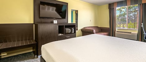 A hotel room with a bed, a TV, a microwave, a sofa, and a window with blinds.