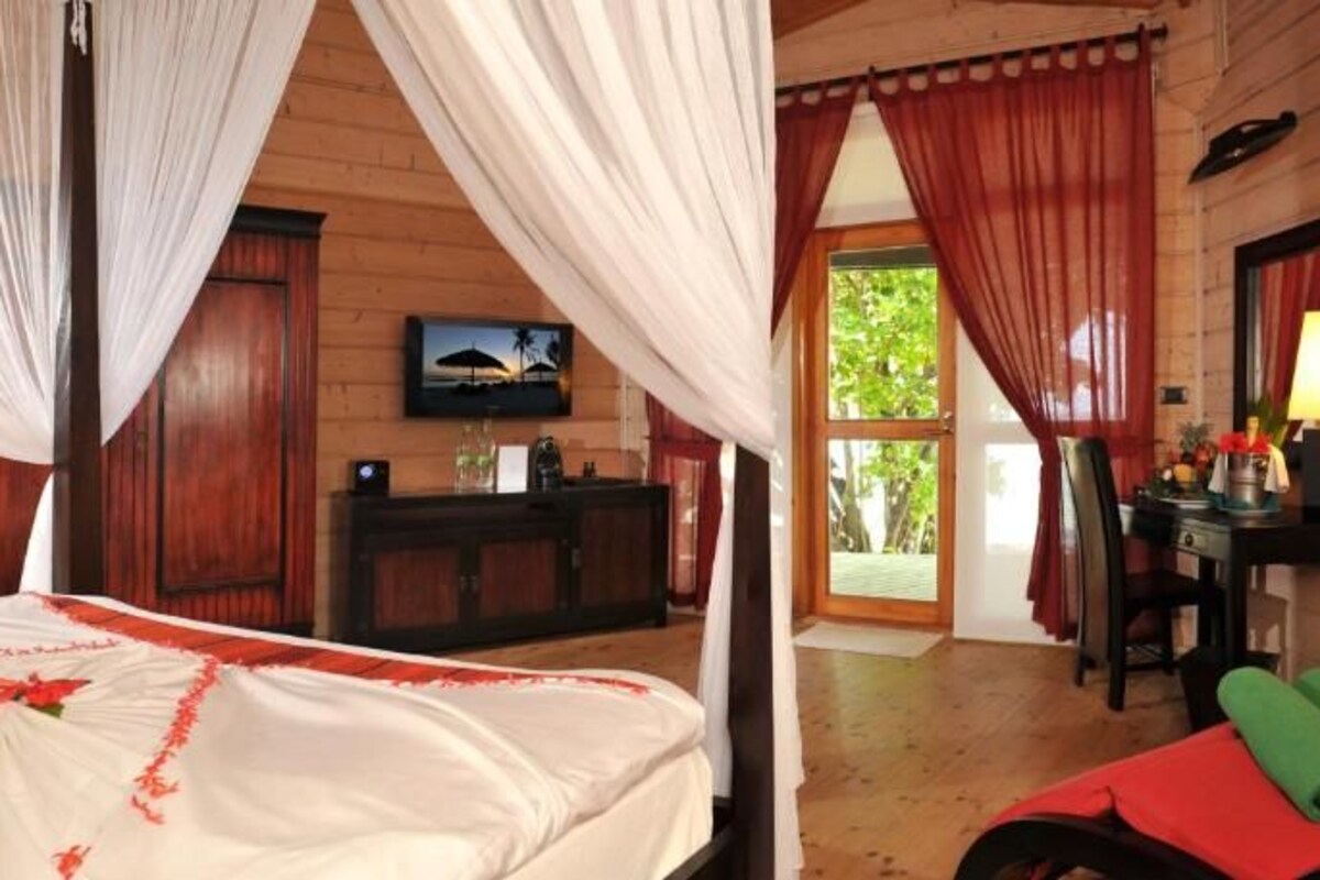 A room with a bed, a TV, a desk, and a window with curtains.