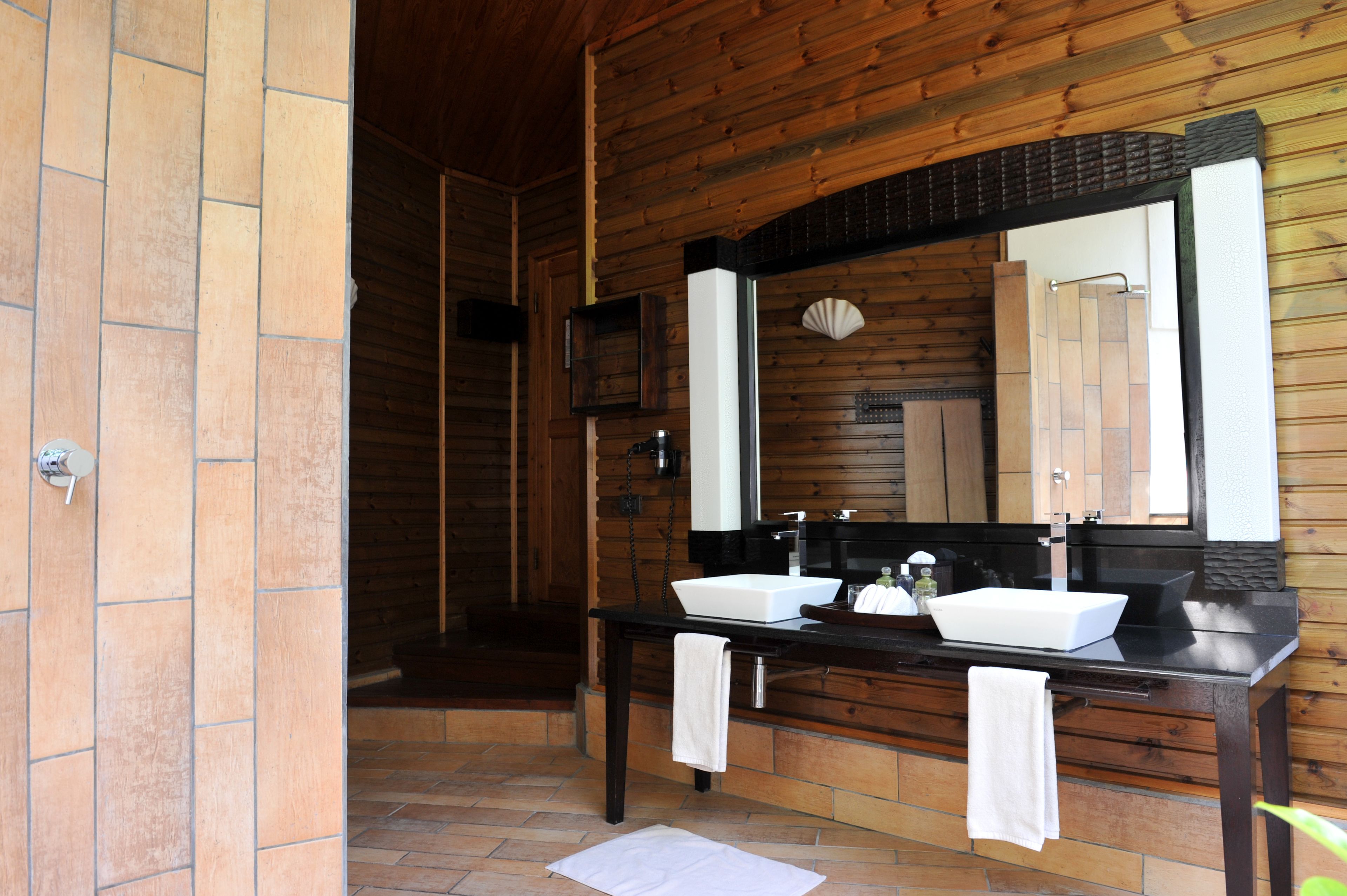 A wooden bathroom with two sinks, a large mirror, and a shower area.