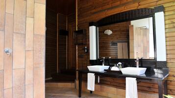 A wooden bathroom with two sinks, a large mirror, and a shower area.