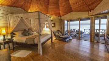A wooden cabin with a four-poster bed, a balcony with outdoor seating, and a view of the water.