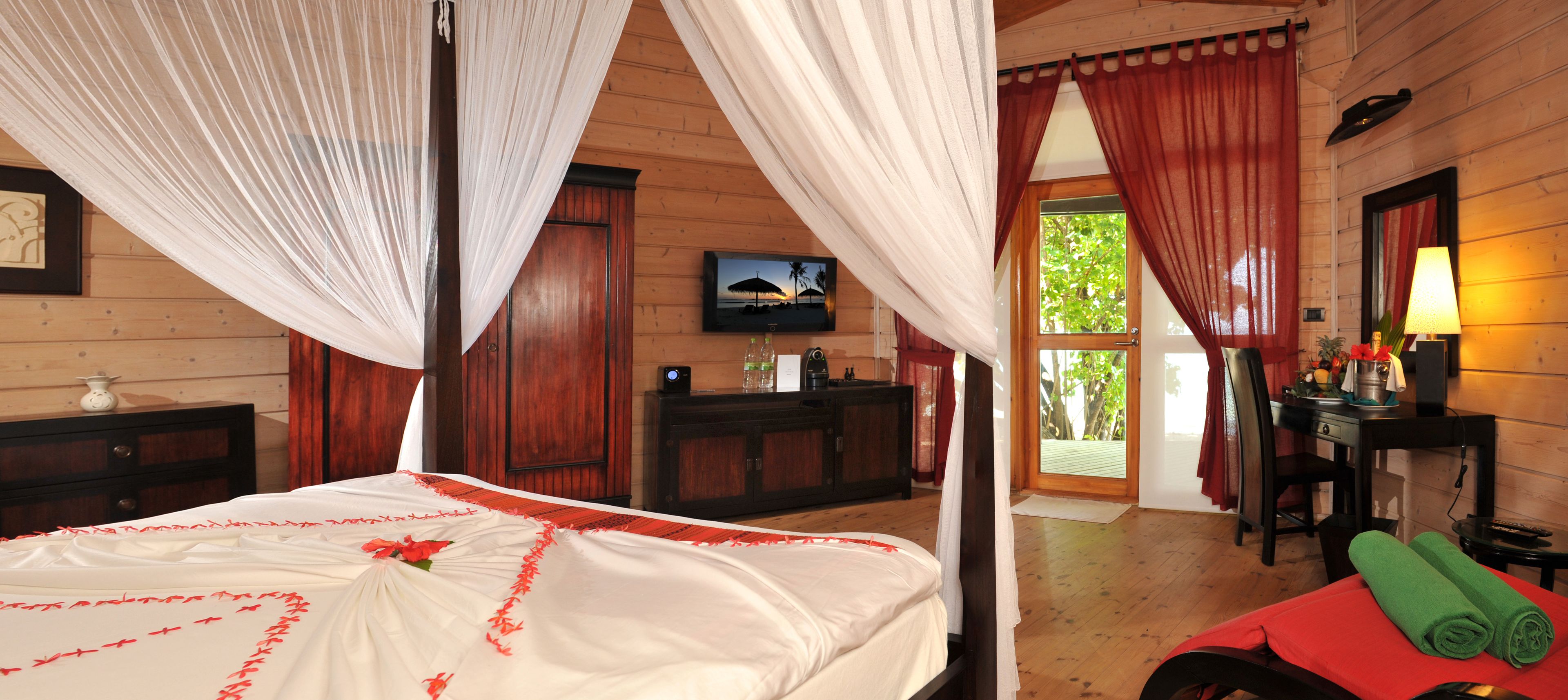 A wooden room with a bed, a desk, a chair, a TV, and a window with curtains.