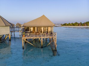 Overwater bungalows offer access to the sea, with large glass doors and windows providing unobstructed views of the surrounding water and sky.