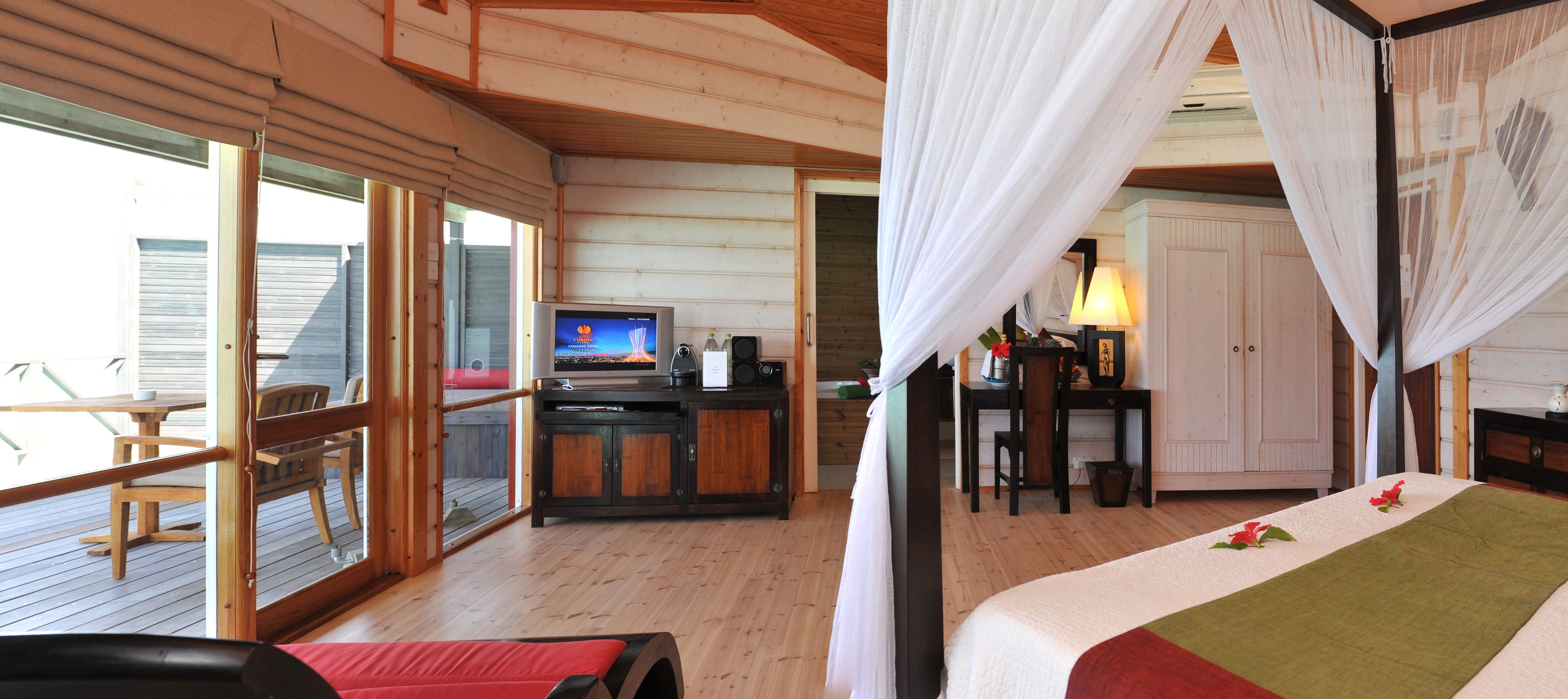 Una habitación con cama, televisión, escritorio y balcón.
