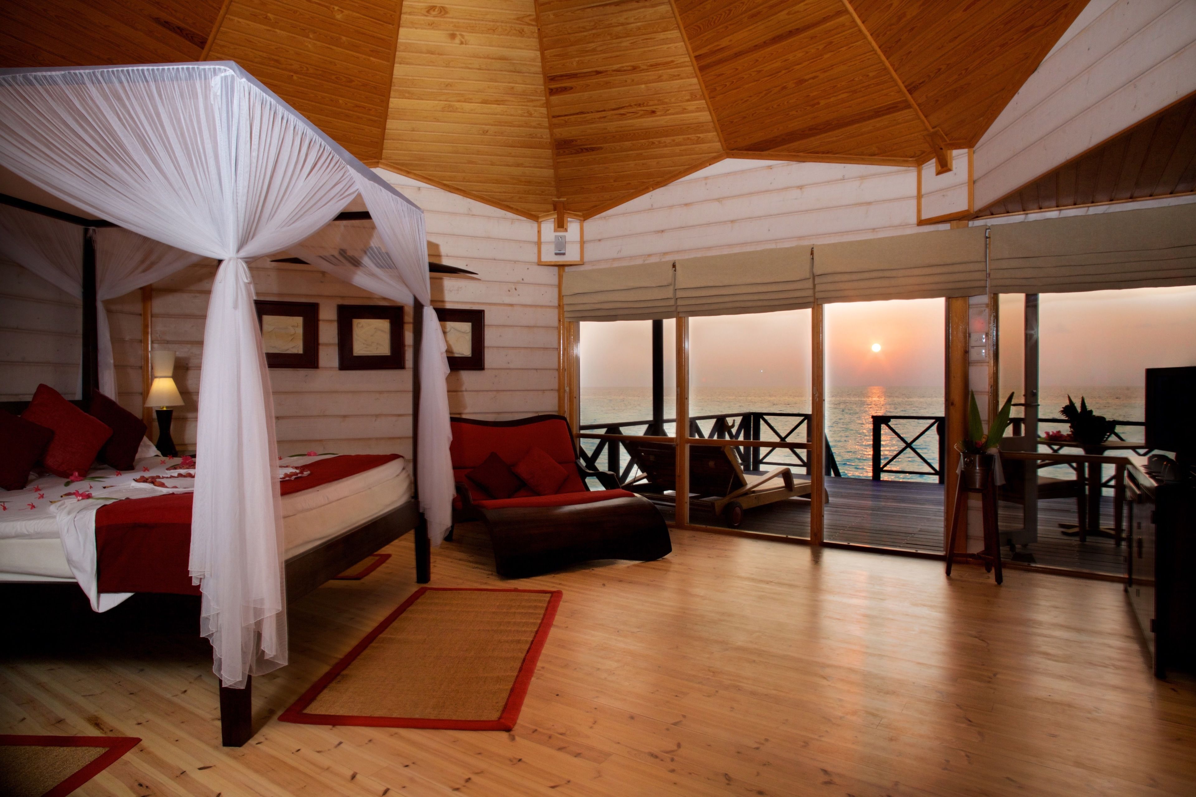 A bedroom with a canopy bed, a balcony with a view of the sunset, and a dining area with outdoor seating.