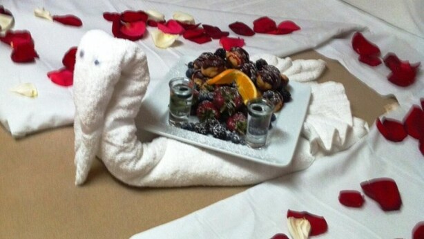 A bed with rose petals and a plate of fruit arranged on it. - Wescana Inn (The Pas)