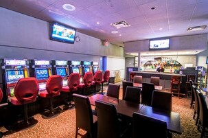 Un casino con múltiples máquinas tragamonedas, una zona de bar y varias mesas y sillas para comer.