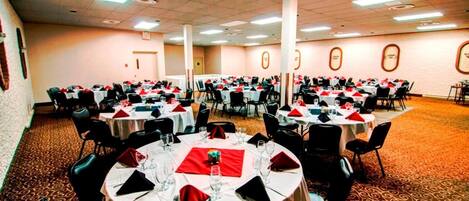 A banquet hall with round tables set for dining, featuring red napkins and white tablecloths.