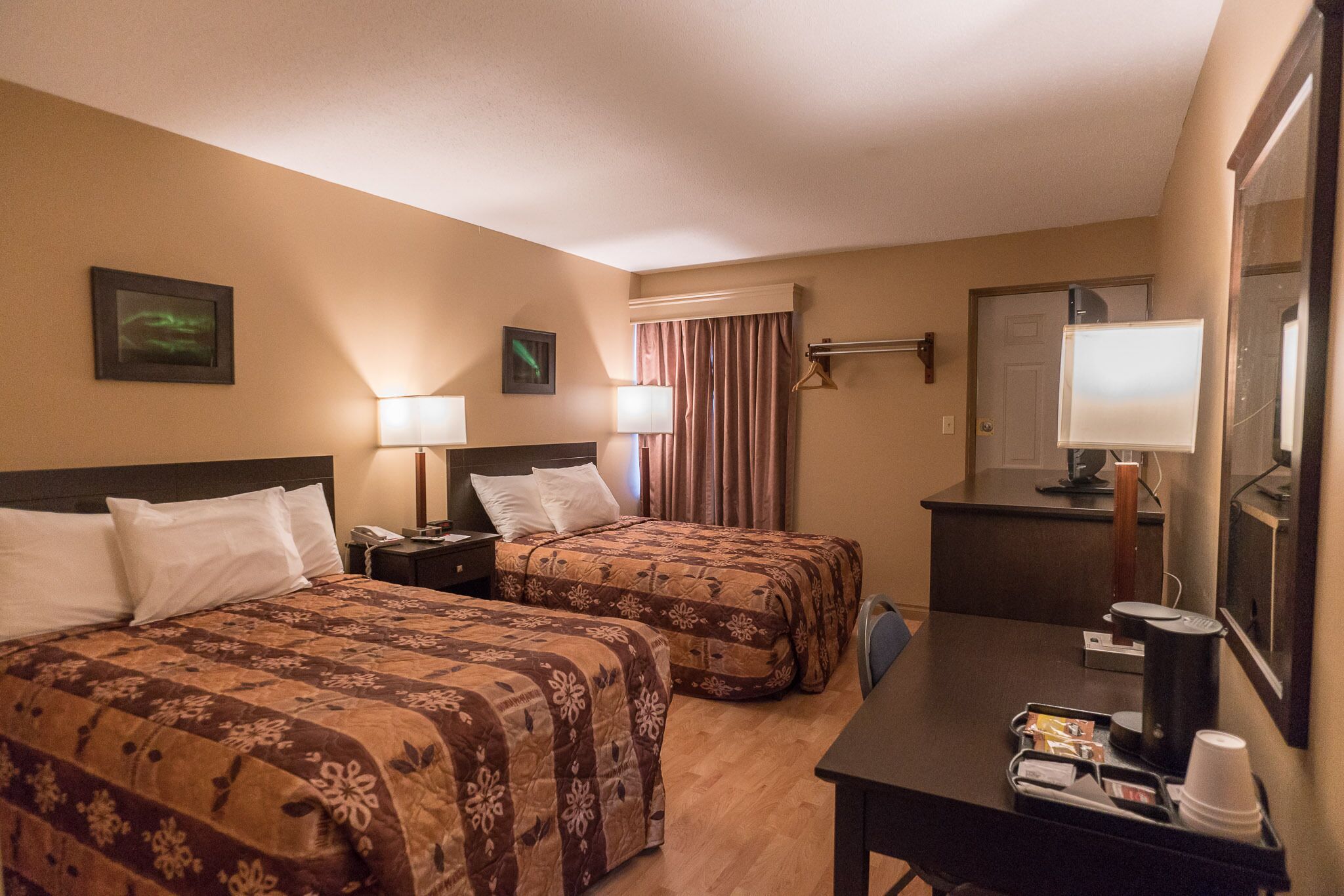 A hotel room with two beds, a desk with a coffee maker, a mirror, and a TV.