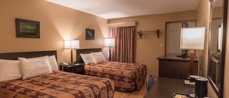A hotel room with two beds, a desk with a coffee maker, a mirror, and a TV.