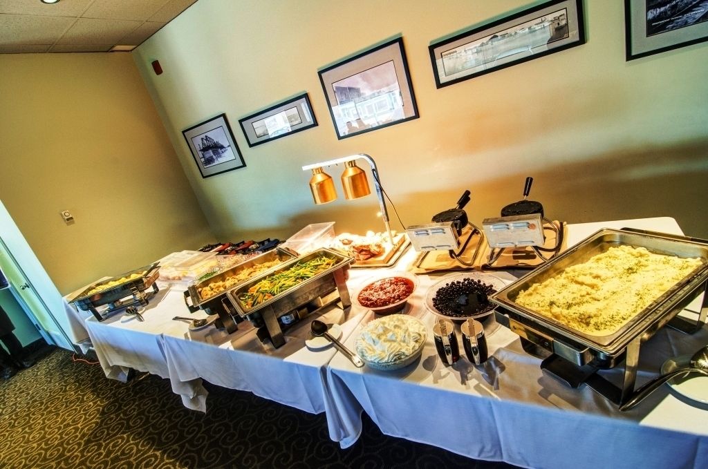 A buffet table with various food items and a coffee station, set in a room with framed pictures on the wall.