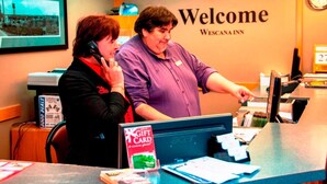 A reception desk with a 'Welcome' sign, a computer, and a 'Gift Card' sign. - Wescana Inn (The Pas)